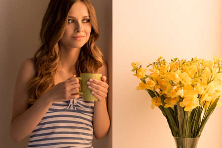 Drinking coffee. Beautiful young woman drinking coffee near the windowの写真素材