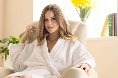 Day off at home. Attractive young woman in bathrobe sitting at the chair and smilingの写真素材