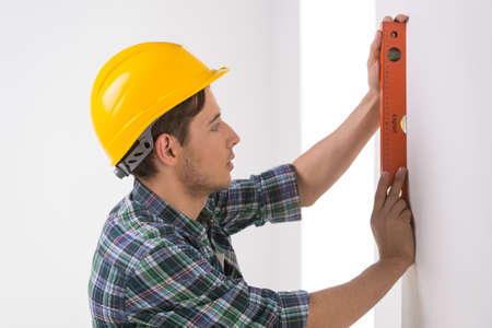 Handyman measuring wall. Confident craftsperson in hardhat measuring the wall levelの写真素材