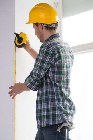 Handyman. Rear view of confident craftsperson in hardhat measuring the wall levelの写真素材