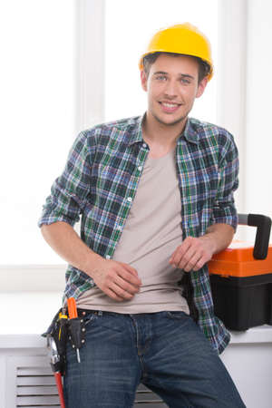 Handyman. Cheerful craftsperson looking at camera and leaning at the windowsillの写真素材