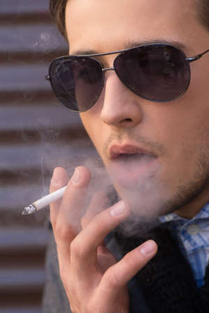 Man smoking. Thoughtful young man in sunglasses smokingの写真素材