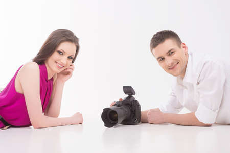 Photographer and model. Young man with camera and fashion model lying face to face and looking at cameraの写真素材