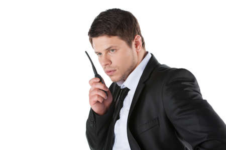 Bodyguard. Confident young man in formalwear talking on radio set while standing isolated on white