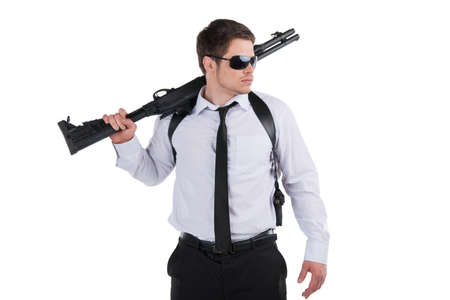 Bodyguard. Confident young man in sunglasses holding gun and looking away while standing isolated on whiteの写真素材