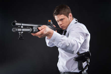 Bodyguard. Serious young man in shirt and tie holding gun and aiming somewhere while standing...
