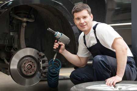 Auto mechanic at work. Cheerful auto mechanic sitting near the car and holding a work toolの写真素材