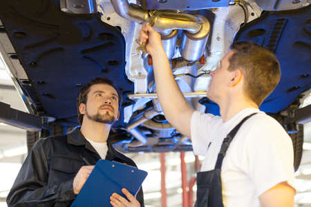 Two mechanics at work. Two confident auto mechanic working at the repair shop while one of them holding a clipboardの写真素材