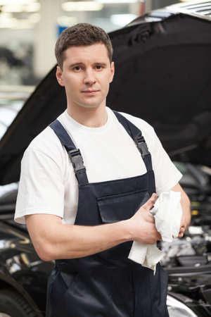 Confident in his work. Close-up of mechanic wiping his hands with handkerchief while standing in front of the carの写真素材