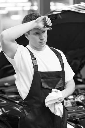 Tired auto mechanic. Tired auto mechanic holding a handkerchief and holding his hand on the foreheadの写真素材