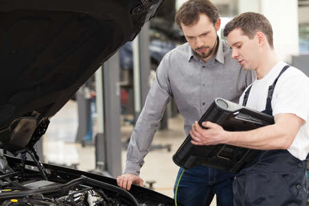 Examining a car. Confident auto mechanic explaining something to a customer while standing near the carの写真素材