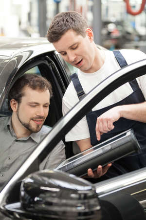 Auto mechanic and car owner. Confident auto mechanic explaining something to a customer sitting at the front seat of carの写真素材