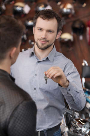 Here is your key. Confident young sales executive giving the key to motorcycle ownerの写真素材