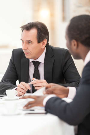Confident mid adult businessman listening to co-worker in conference roomの写真素材