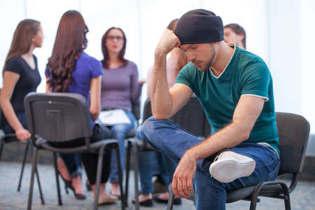Young man is in deep depression. Trying to solve his problems. Group of people discussing something on backgroundの写真素材