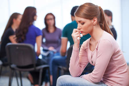 Young upset woman on foreground. Group of people talking on backgroundの写真素材