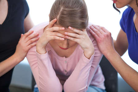 Two women comforting crying girl. Close up of crying girl, who covers her face with both handsの写真素材