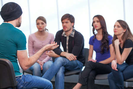 Young man is holding seminar. Four people listening to a man while sittingの写真素材