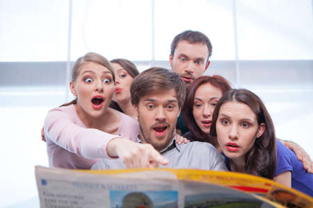 Group of young people reading newspaper. Looking very surprised and interested inの写真素材