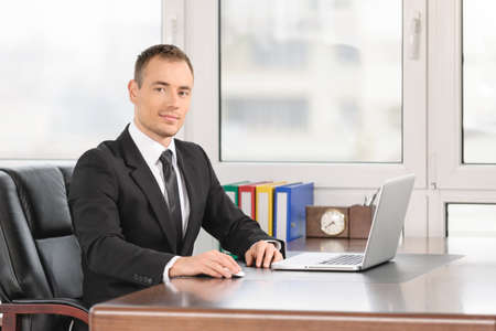 Businessman sitting at his desk with laptopの写真素材