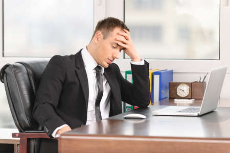 Businessman looking down with laptop at officeの写真素材