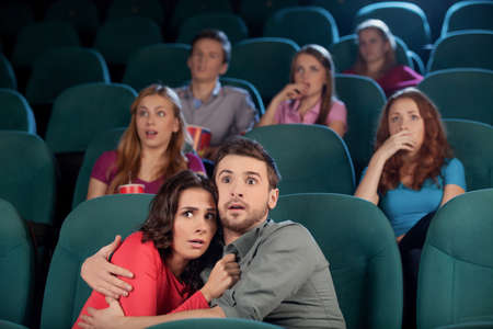 Horror movie. Terrified young couple hugging while watching movie at the cinemaの写真素材