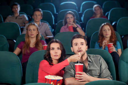 Great movie! Young couple feeding each other while watching movie at the cinemaの写真素材