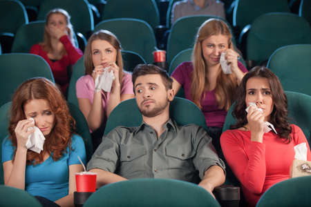 Watching drama. Handsome young men looking bored while women crying during the movie session in the...