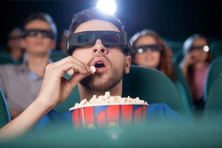 Men at the cinema. Excited young men in glasses watching movie at the cinema and eating popcorn