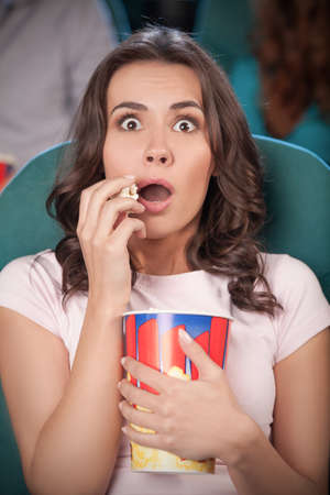 Women at the cinema. Beautiful young women eating popcorn while watching movie at the cinemaの写真素材