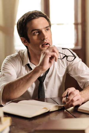 Waiting for inspiration to strike. Handsome young author sitting at the table with a pen in his hand and waiting for inspirationの写真素材