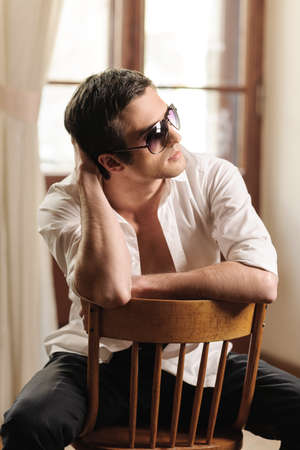 Cool and handsome. Handsome young men in sunglasses sitting on the chair leaning his head on handの写真素材
