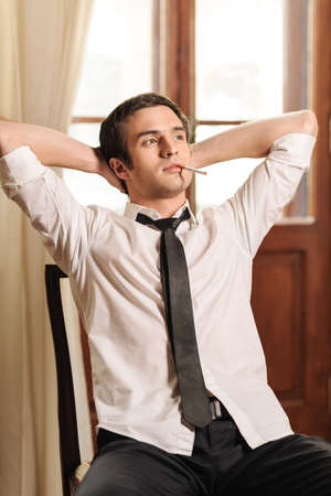 Happy with his life going. Handsome young men in necktie sitting on the chair with his head in handsの写真素材