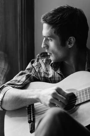 Looking for inspiration outside. Black and white shot of men playing guitar and looking through windowの写真素材