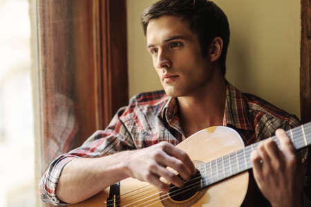 He loves the guitar sounds. Handsome young men sitting on the windowsill and playing guitarの写真素材
