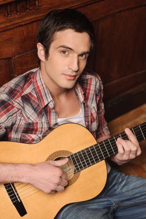 Music makes him happy. Handsome young men sitting on the floor and playing guitarの写真素材