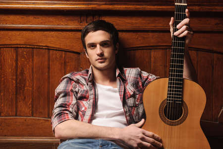 Men and his guitar. Handsome young men sitting on the floor and holding his guitarの写真素材