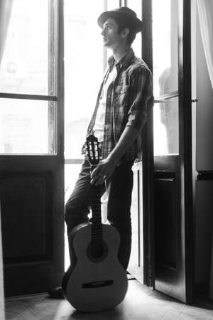 The street needs my music. Handsome young men holding an acoustic guitar and looking through the open doorの写真素材