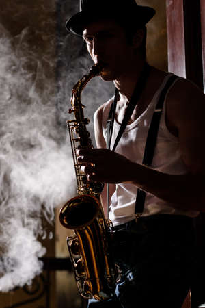 Jazz is his life. Handsome young jazzmen playing sax with a smoke on the backgroundの写真素材