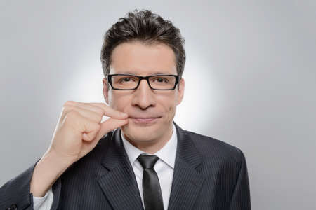 No more word. Portrait of confident businessman holding his finger on the lips and looking at cameraの写真素材