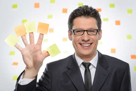 Multi-tasking businessman. Portrait of cheerful businessman showing his hand with sticky notes on each fingerの写真素材
