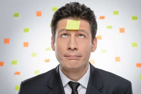 Itï¿½ so much to do. Portrait of frustrated businessman looking up on the adhesive note attached to his foreheadの写真素材