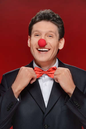 Funny man. Portrait of cheerful man with a clown nose touching his bow tie and looking at cameraの写真素材