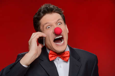 He is not taken seriously. Portrait of angry man with a clown nose touching talking at phone and...