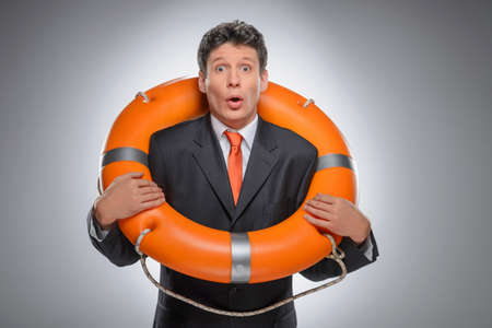 Businessman with a life buoy  Surprised businessman standing with a life buoy while isolated on grayの写真素材