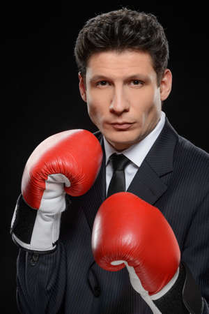Business fighter. Portrait of confident businessman in red boxing gloves standing against black backgroundの写真素材