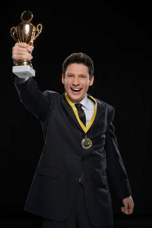 His first business award. Happy businessman showing off a trophy while standing against black backgroundの写真素材