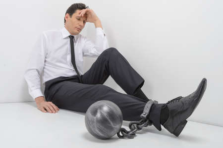 Chained businessman  Full length of depressed businessman sitting on the floor with shackles chained to his legsの写真素材
