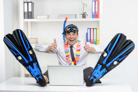 Ready for vacation   Cheerful businessman in flippers and snorkel sitting at his working place and smiling at cameraの写真素材
