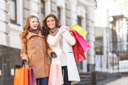 She knows where are the best prices. Two beautiful young women standing with shopping bags in their hands while one of them pointing awayの写真素材